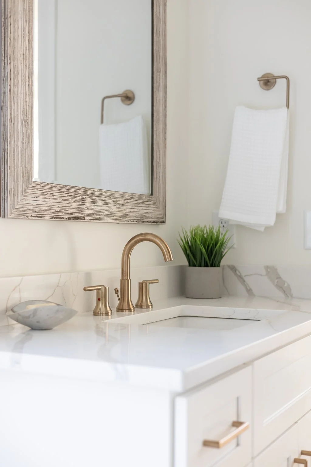 Bathroom vanity with a gold faucet, a wood framed mirror, and a small potted plant