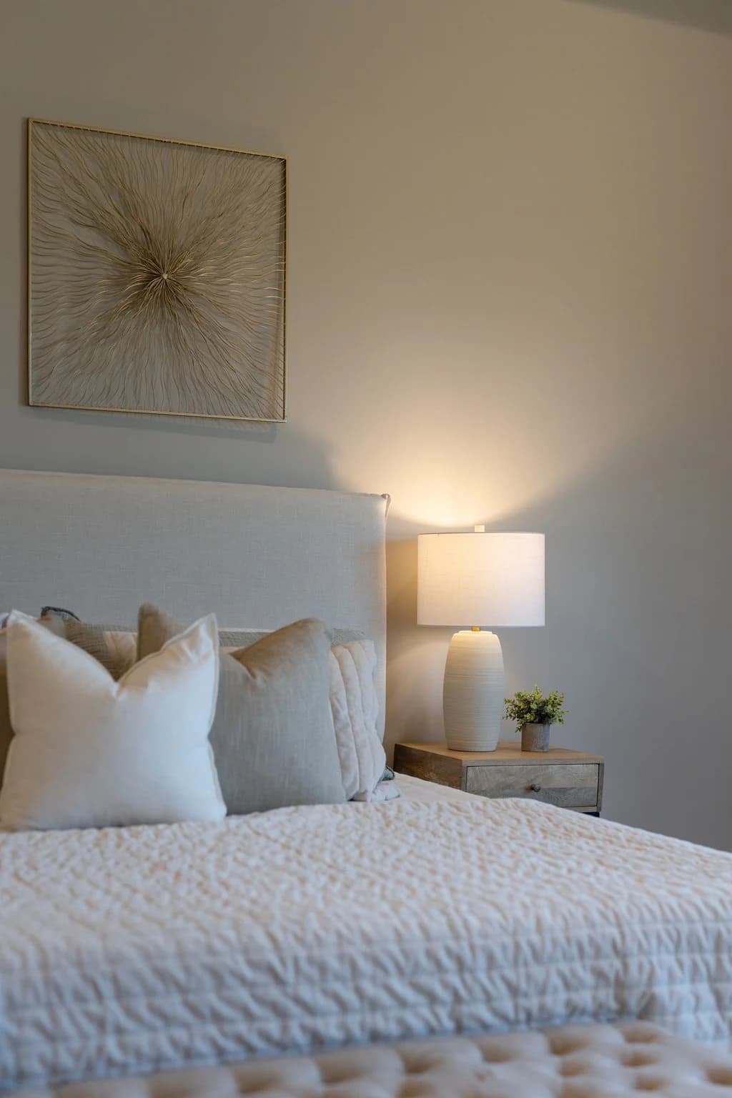 Upholstered bed with cream pillows under gold starburst art and a white lamp
