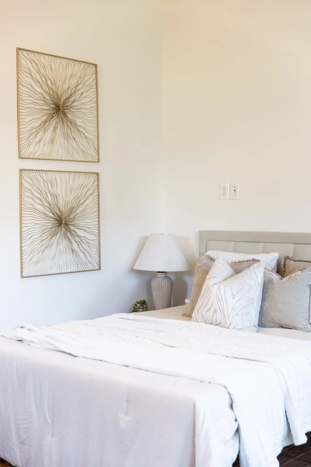 Bed with white bedding and neutral pillows below two gold starburst wall pieces