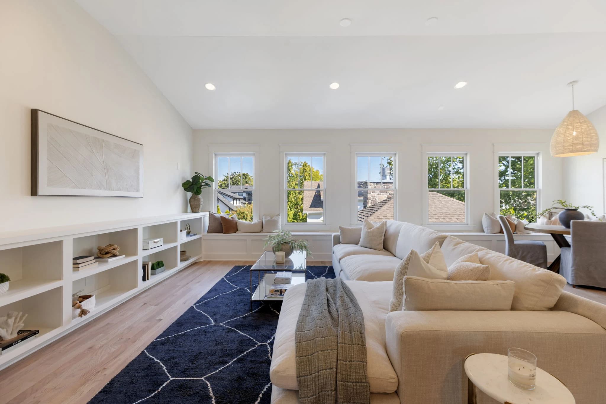 Bonus room with a long white built-in, a cream sectional, a navy rug, and a row of windows
