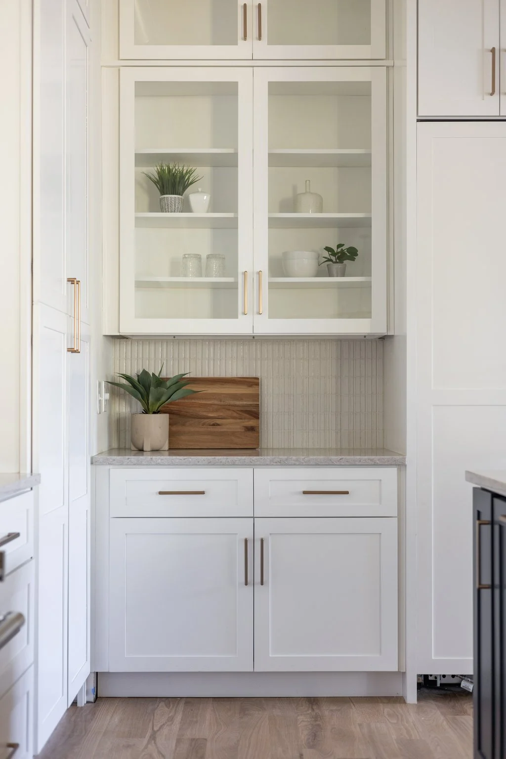 Butler's pantry with glass-front upper cabinets styled with greenery and a wood cutting board