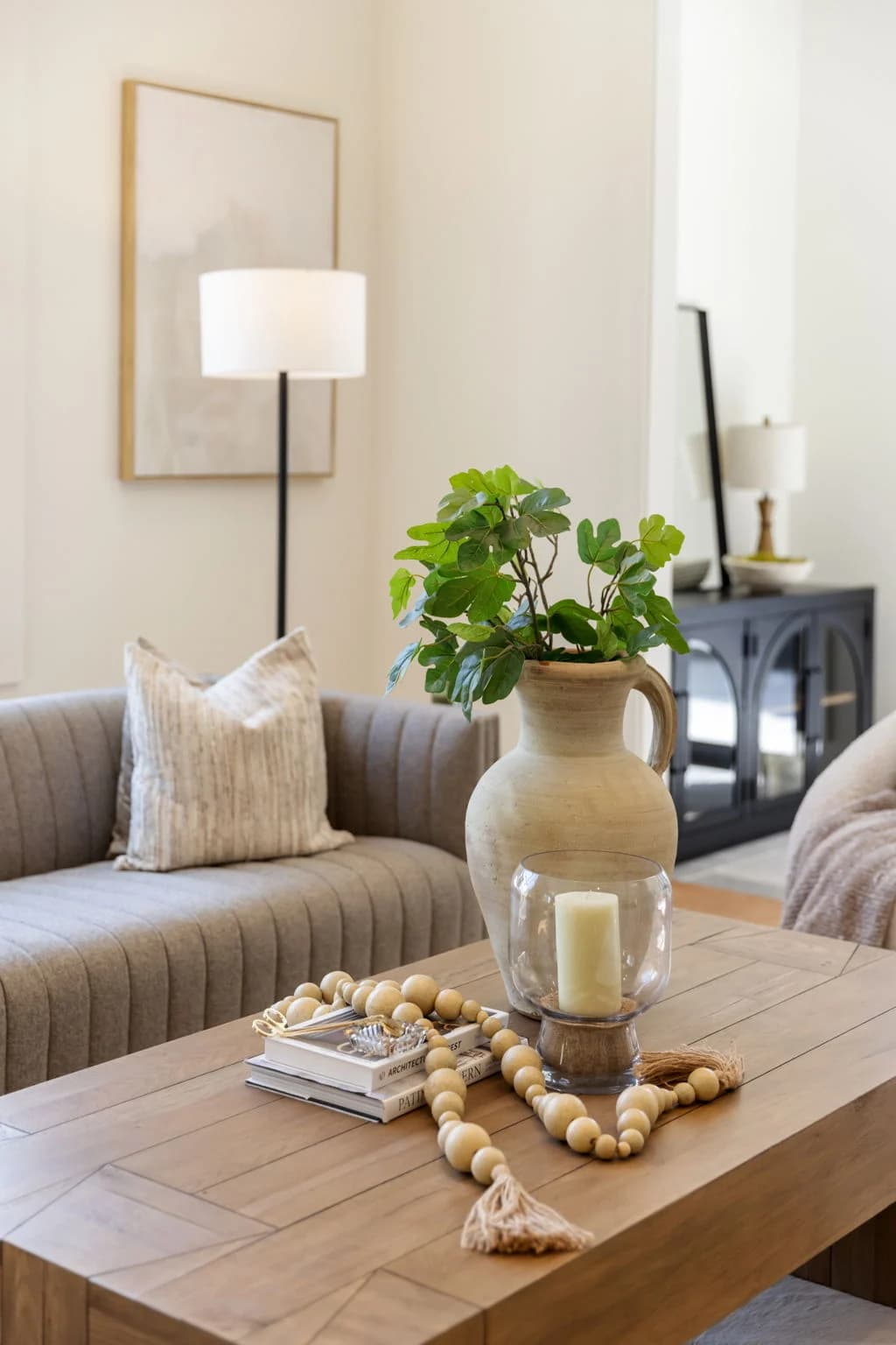Wood coffee table styled with a clay vase, wood bead garland, and a glass candle holder in front of a channel tufted sofa
