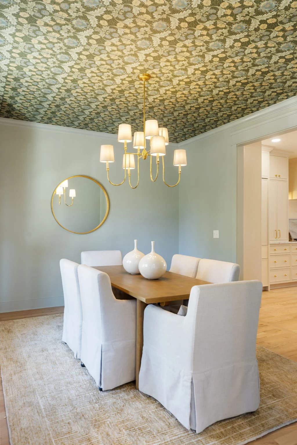 Dining room with a patterned wallpaper ceiling, a brass chandelier, a wood table, and white slipcovered chairs