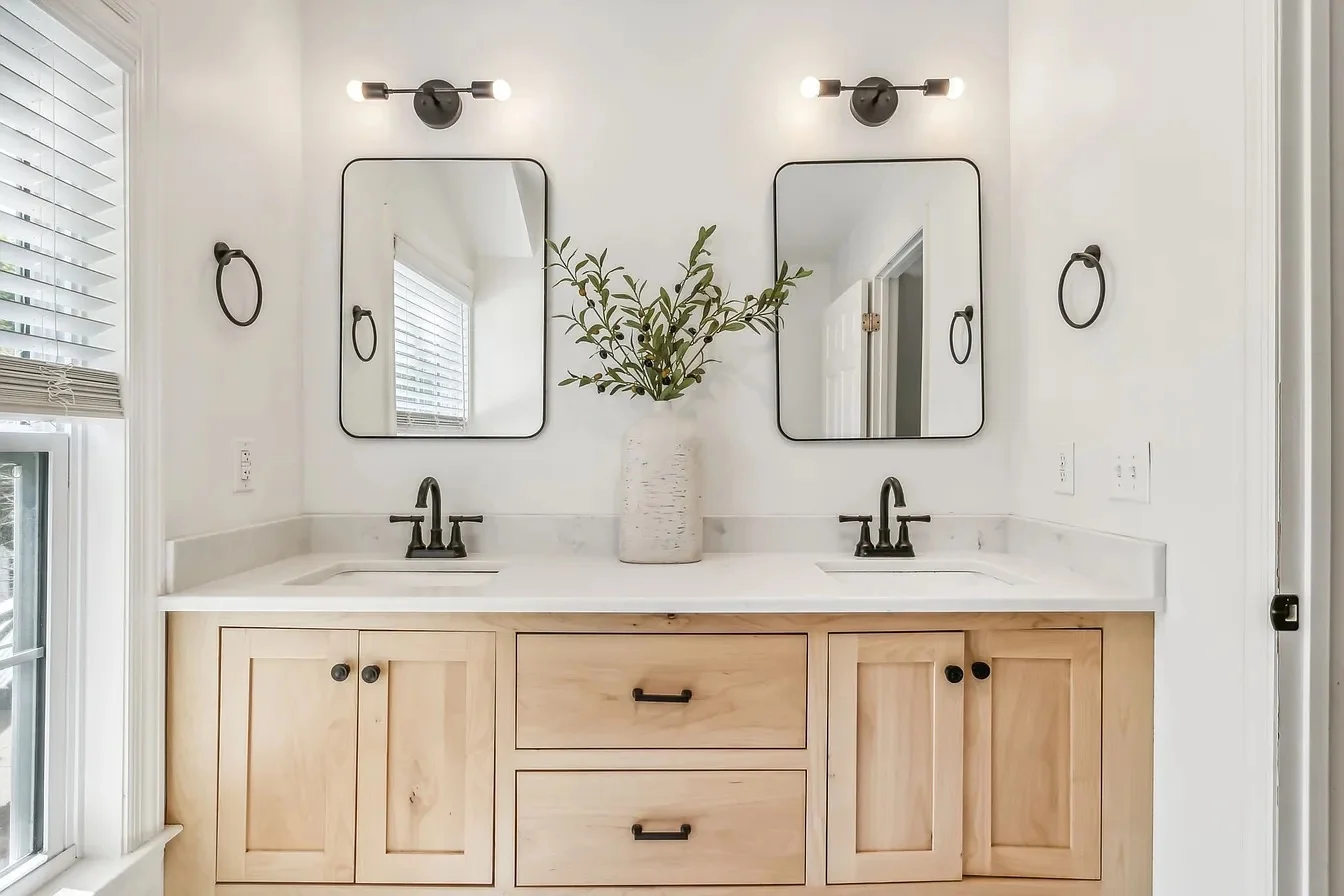 Double vanity bathroom with light wood cabinets and black framed mirrors