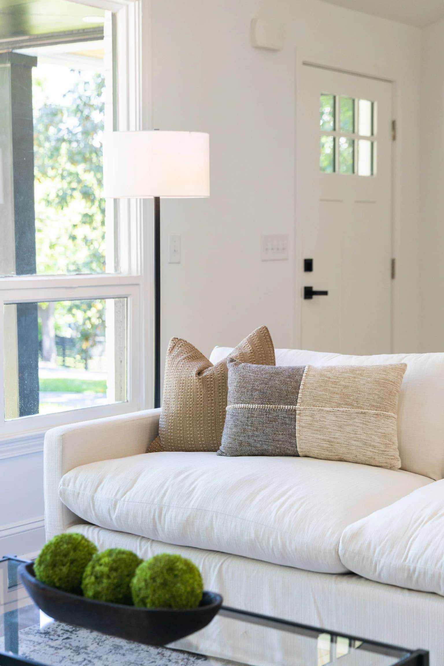 White sofa with neutral pillows near a front door and a floor lamp
