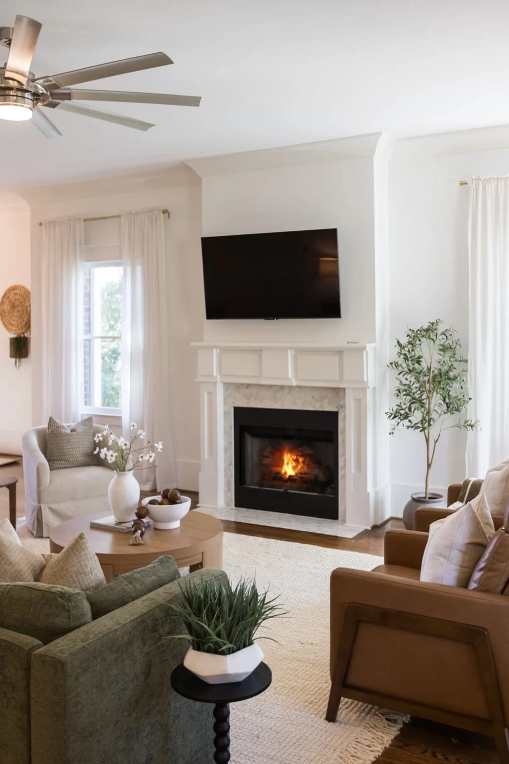 Family room with a lit fireplace, mounted TV, olive sofa, and cognac leather chair