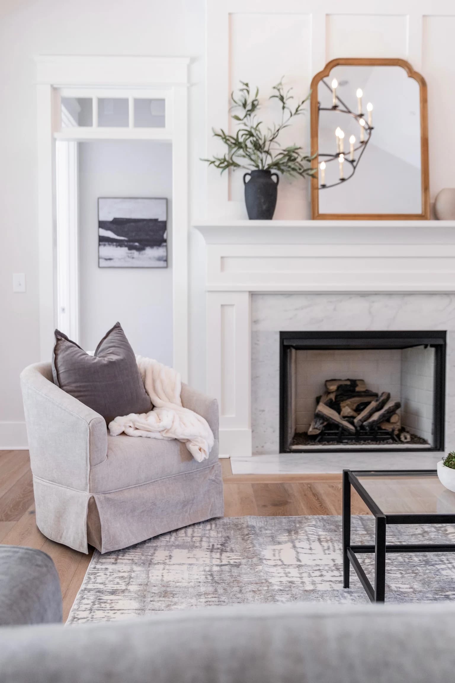 Slipcovered swivel chair beside a white marble fireplace