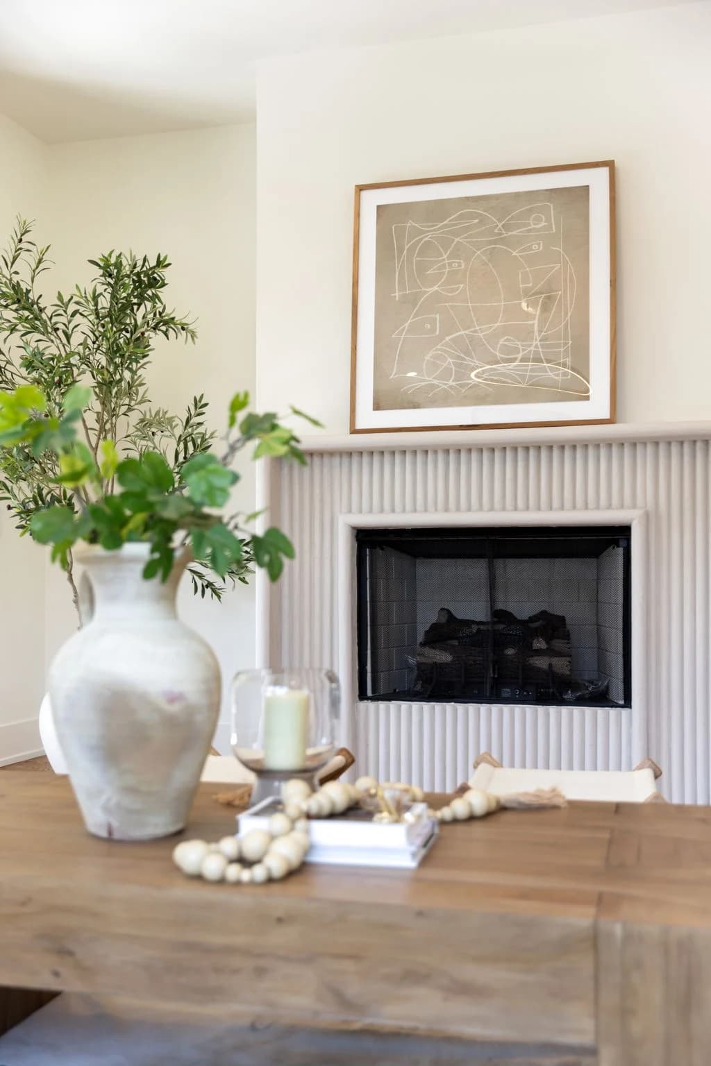 Fluted fireplace with framed abstract art, styled with a clay vase of branches on a wood coffee table