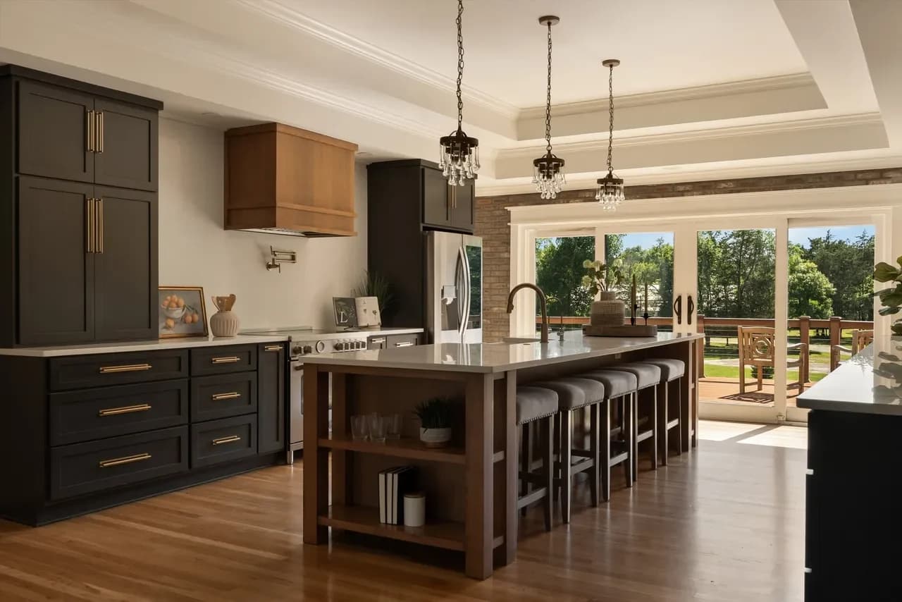 Kitchen with black cabinets, a wood island with counter stools, crystal pendants, and sliding doors to a deck