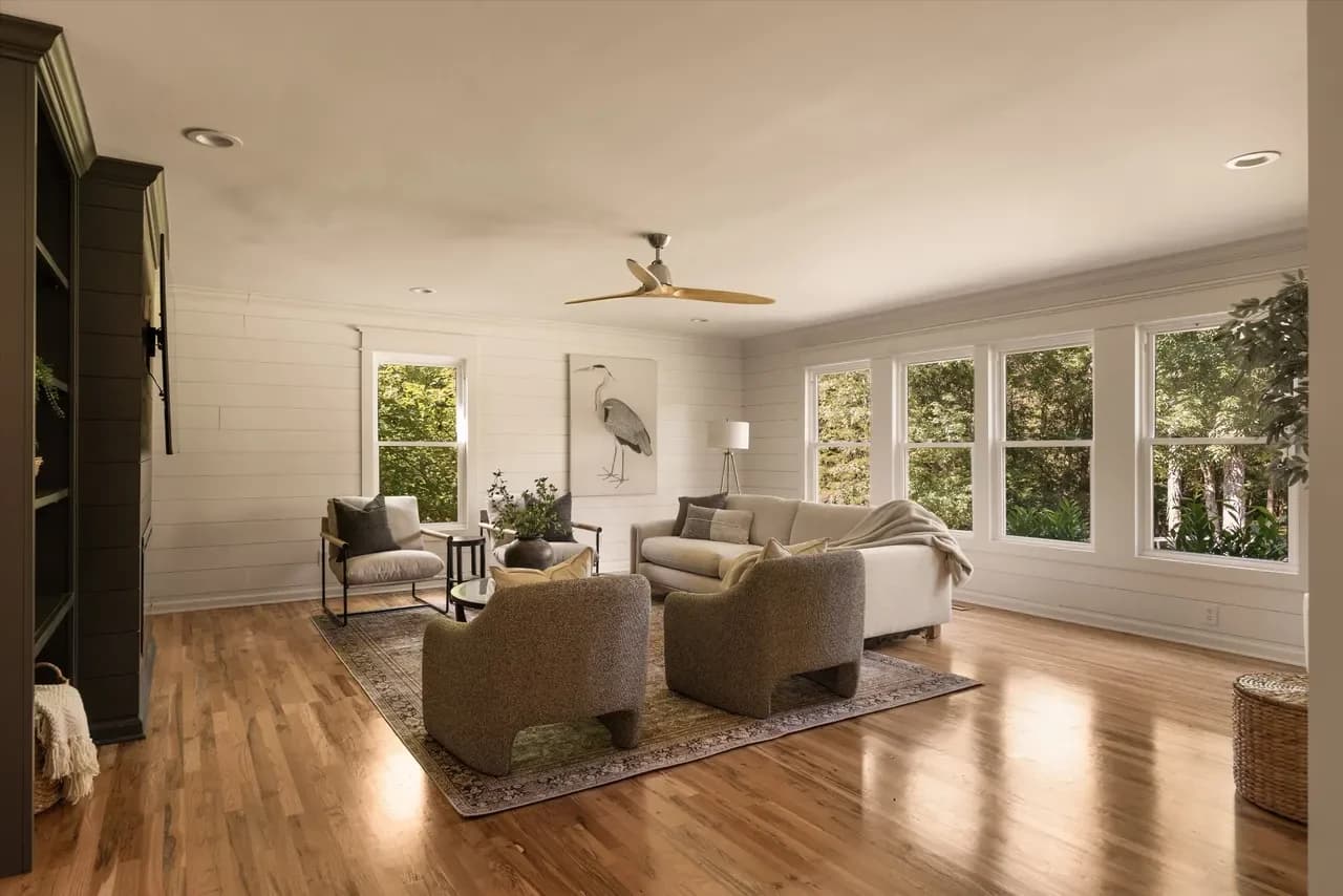 Wide view of a living room with two boucle armchairs on a vintage rug, a cream sofa, and a wood ceiling fan