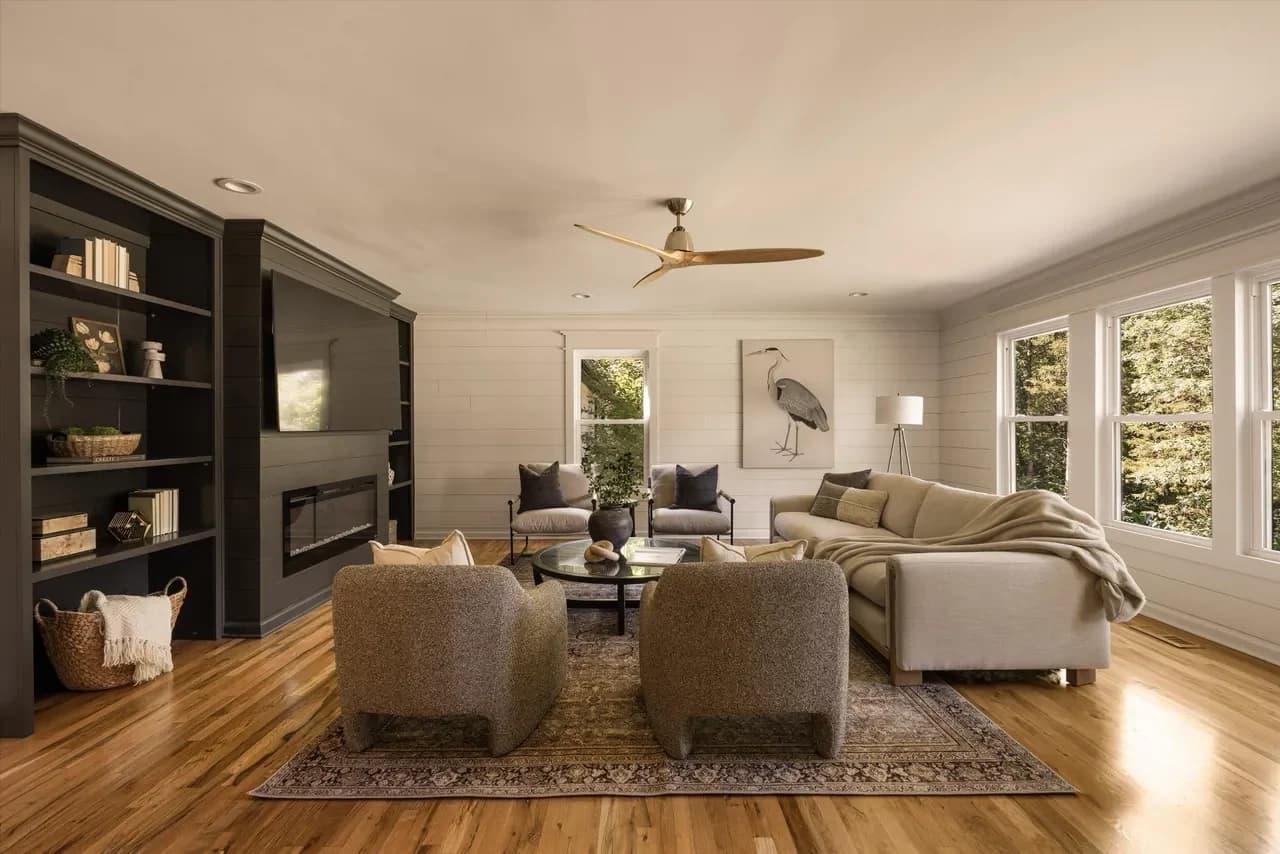 Living room with a dark built-in bookcase and linear fireplace, two boucle armchairs, a cream sectional, and heron art between shiplap walls