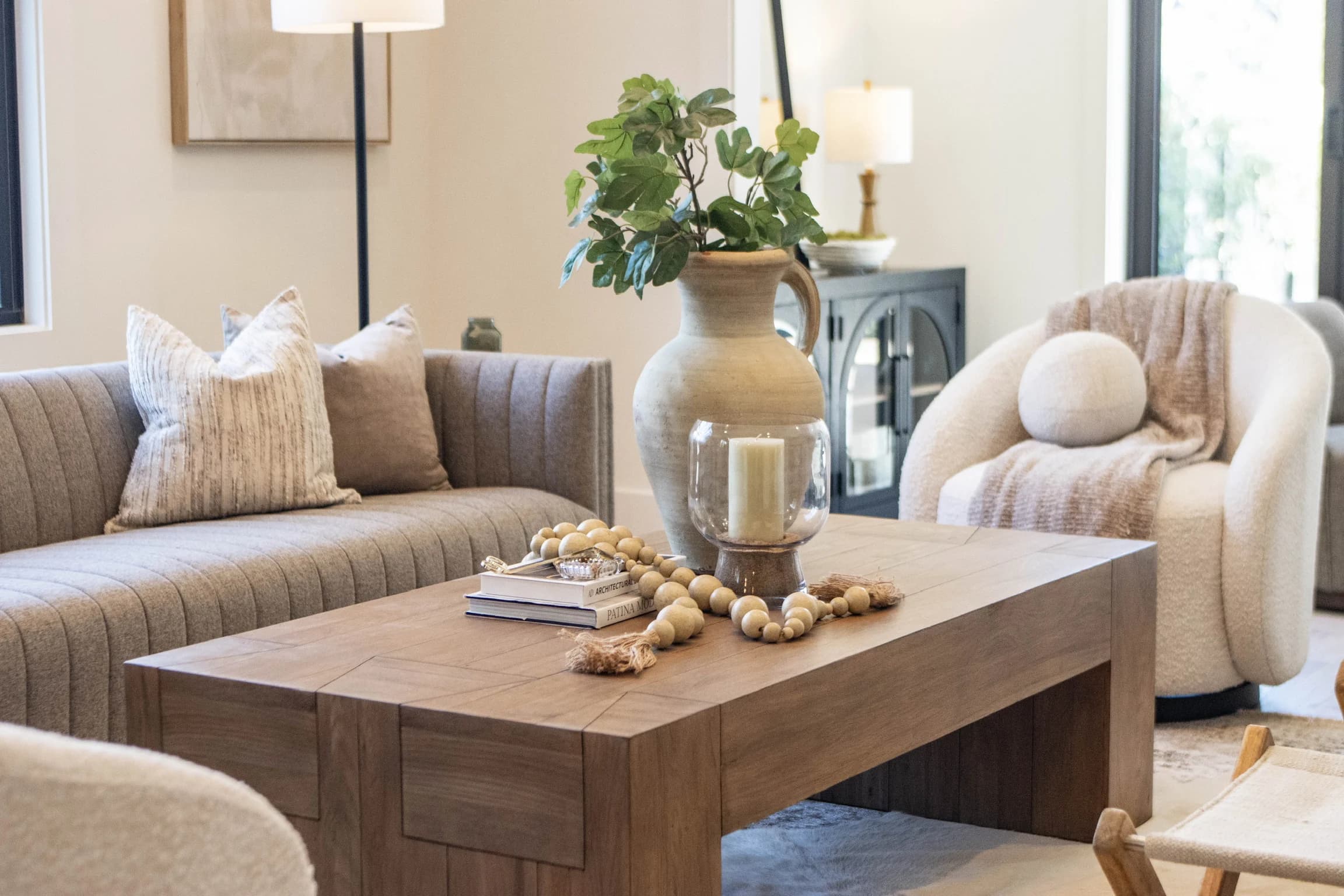 Living room with a channel tufted sofa, a wood coffee table styled with a large vase, and a boucle swivel chair