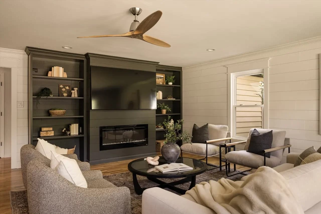 Sofa and two accent chairs around a round black coffee table facing dark built-ins with a linear fireplace