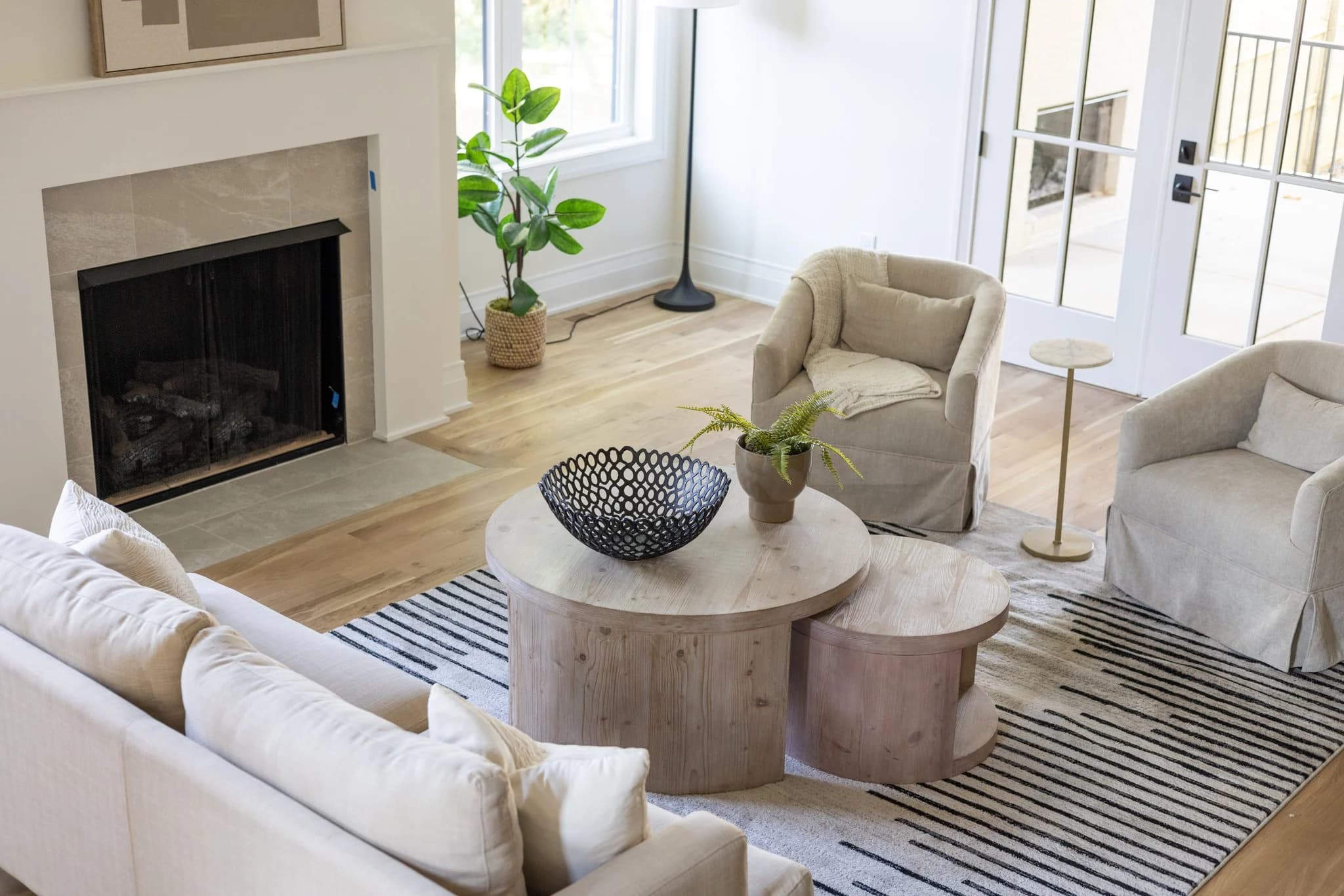 Living room with a fireplace, cream sofa, nesting round wood coffee tables, and a striped rug