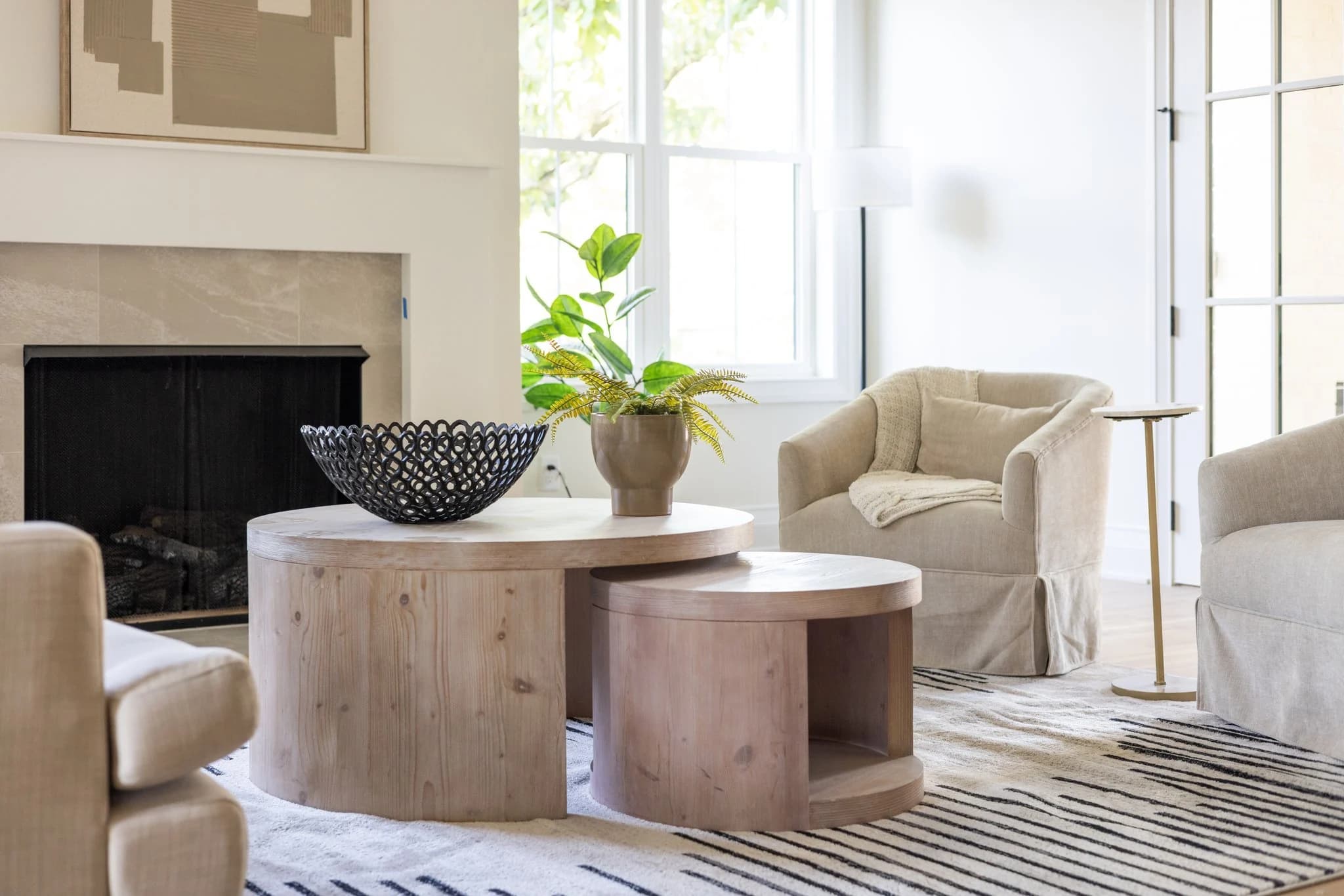 Close view of round wood nesting coffee tables styled with a woven bowl in front of a fireplace