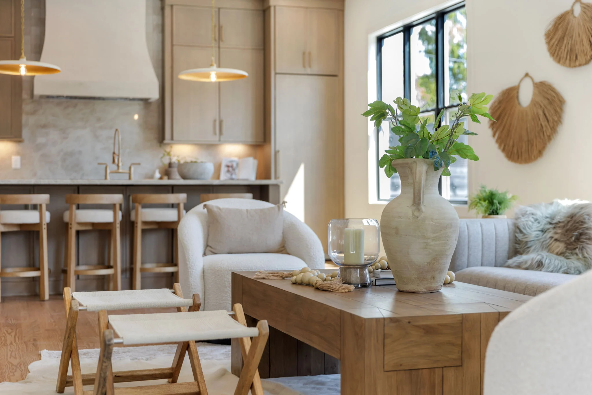 Living room with a boucle swivel chair and a wood coffee table styled with a clay vase of greenery, open to a kitchen with oak cabinets and pendant lights