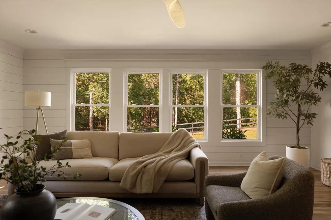 Shiplap living room with a cream sofa, a draped throw, and a row of windows looking out to tall trees