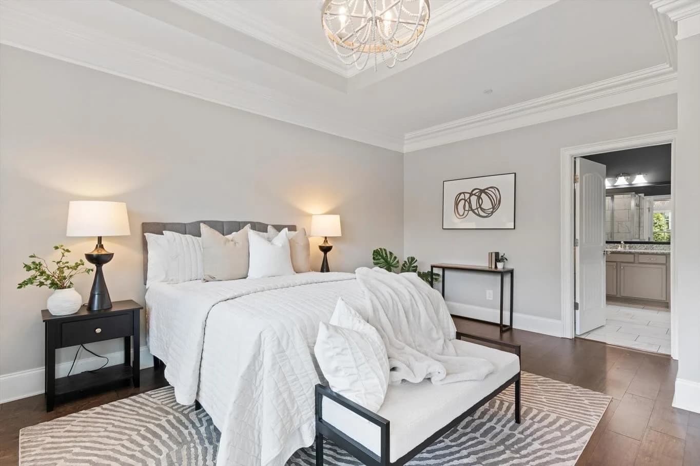 Primary bedroom with a white bed, black nightstands, and an upholstered bench on a zebra rug