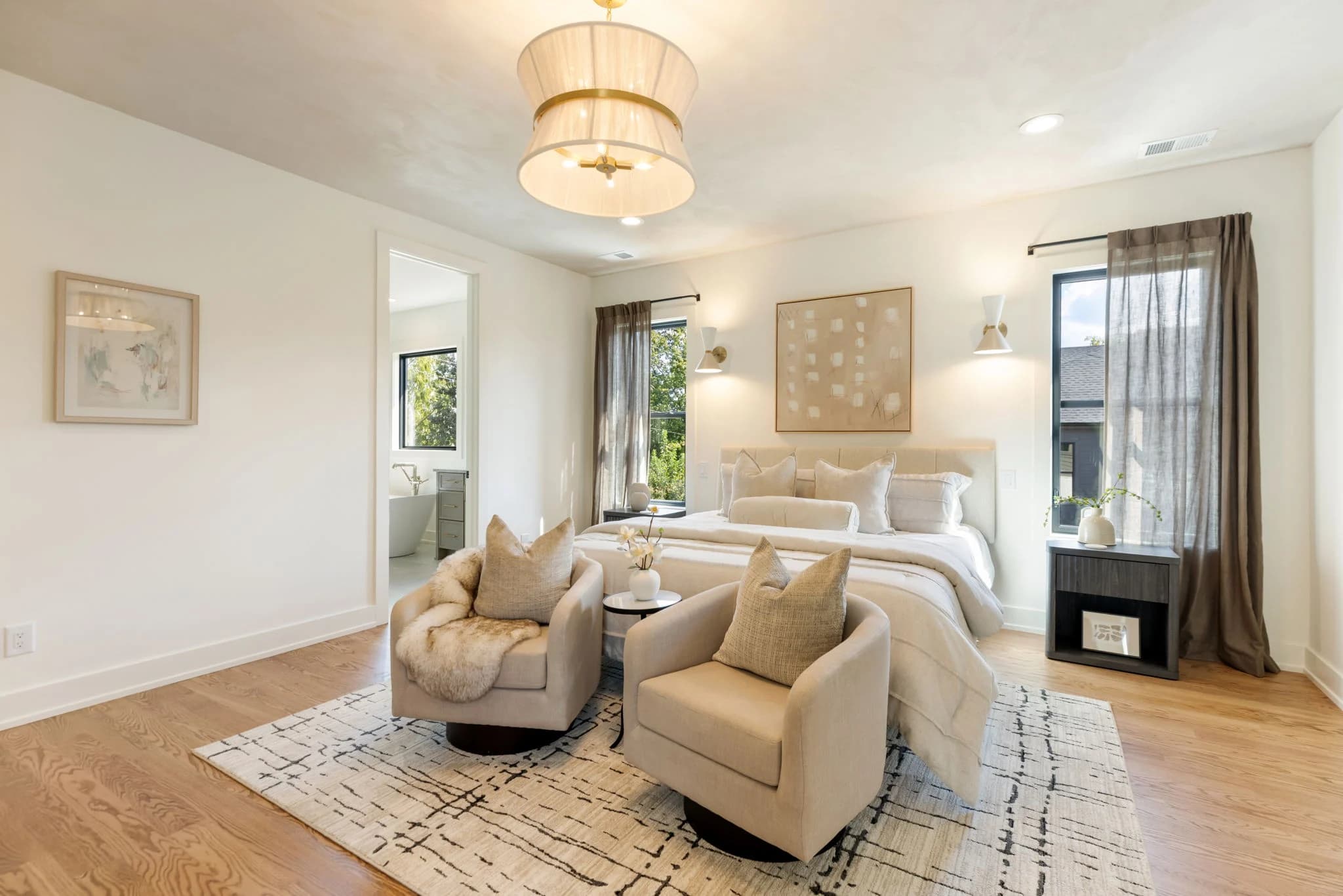 Primary bedroom with two cream swivel chairs at the foot of the bed, a drum chandelier, and sheer drapes