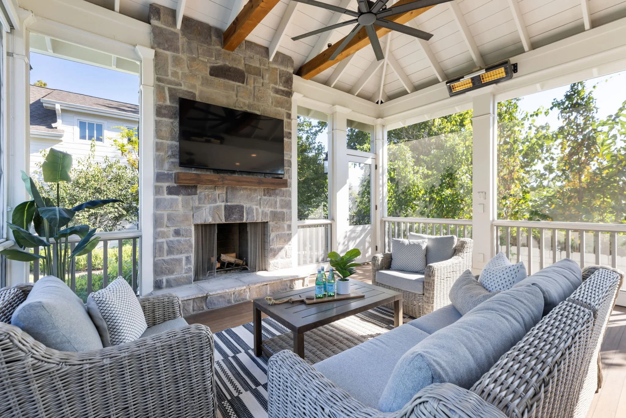 Screened porch with a stone fireplace, wicker sofas with blue cushions, and a vaulted beamed ceiling