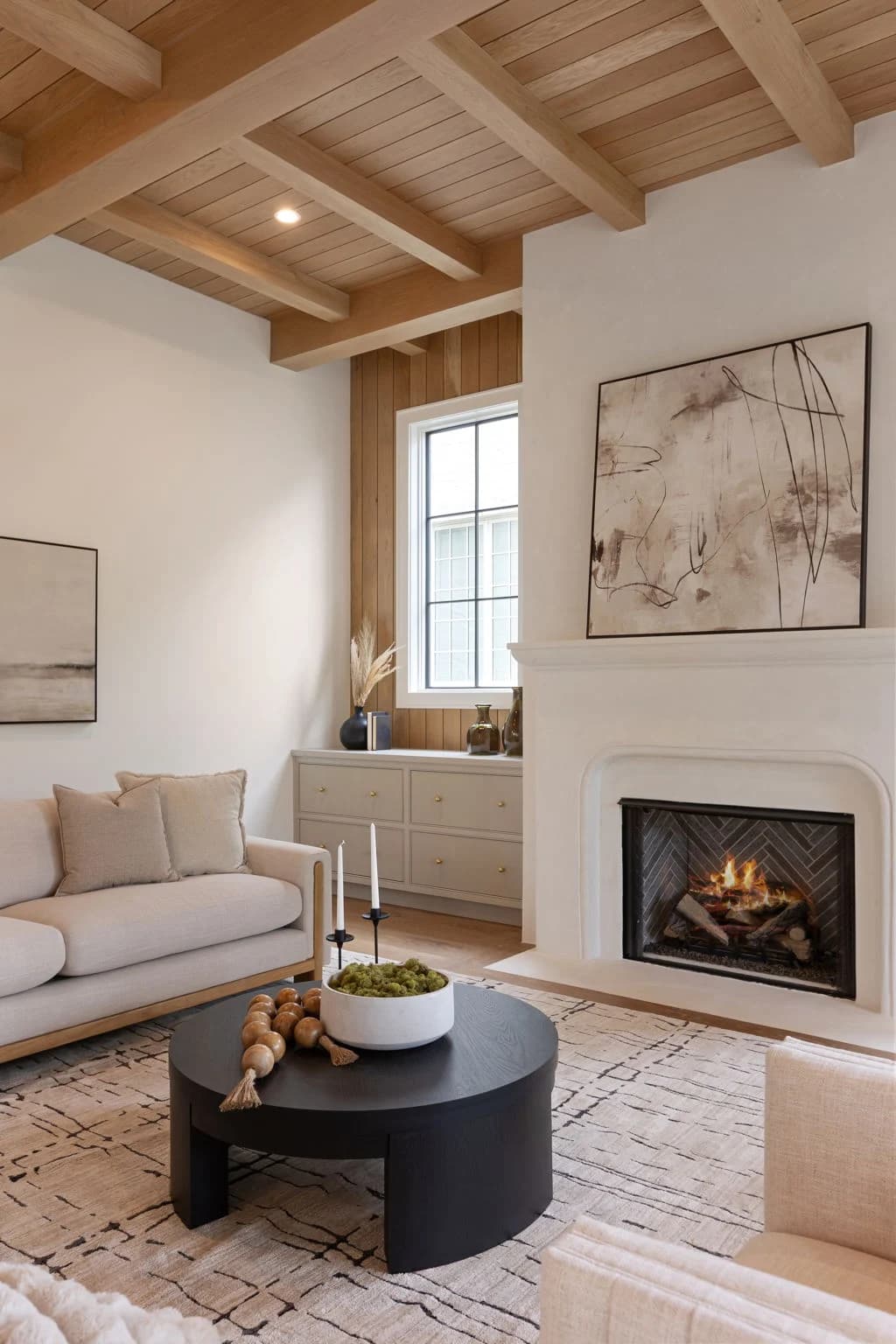 Sitting room with a loveseat facing a lit plaster fireplace, a round black coffee table, and a patterned rug