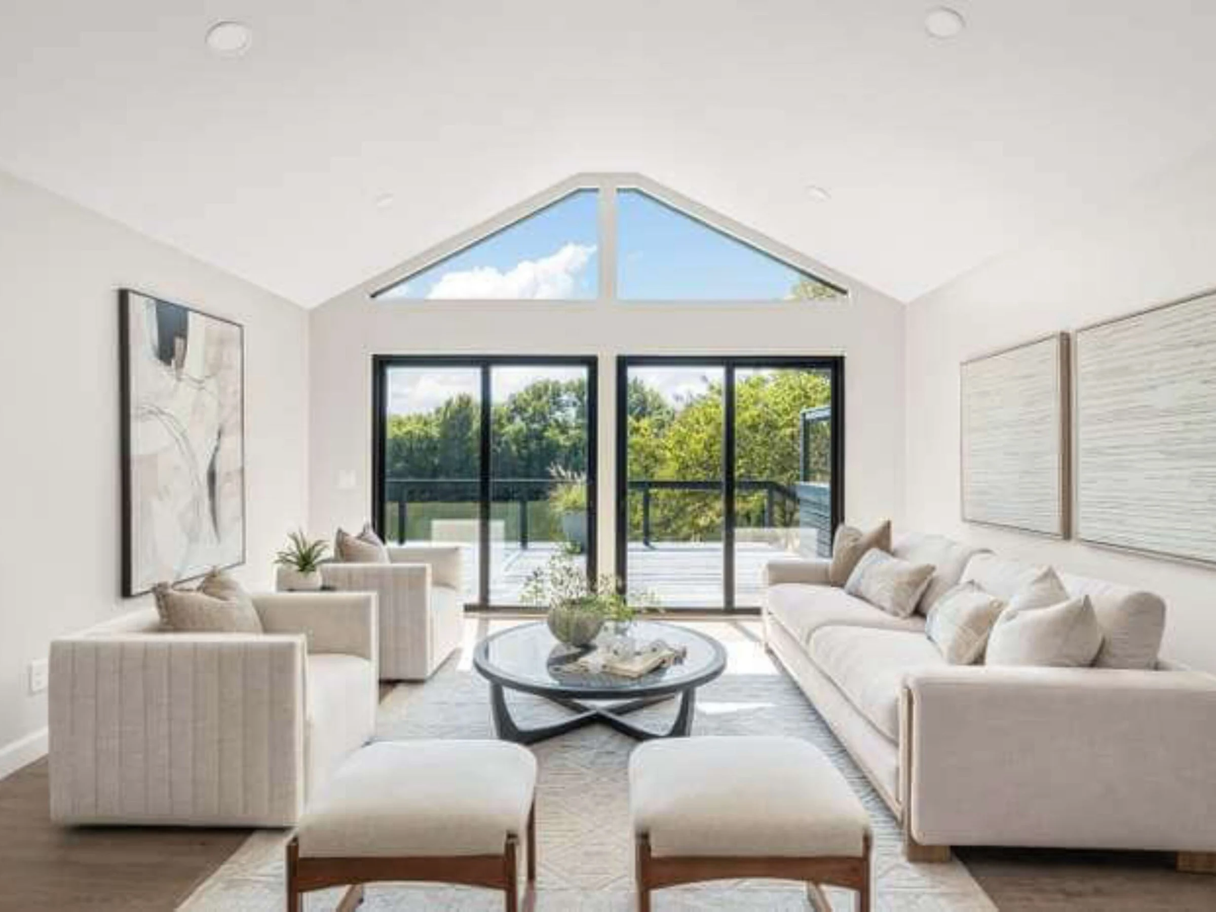 After staging: the same vaulted living room with cream sofas, two ottomans, a round coffee table, and large abstract art