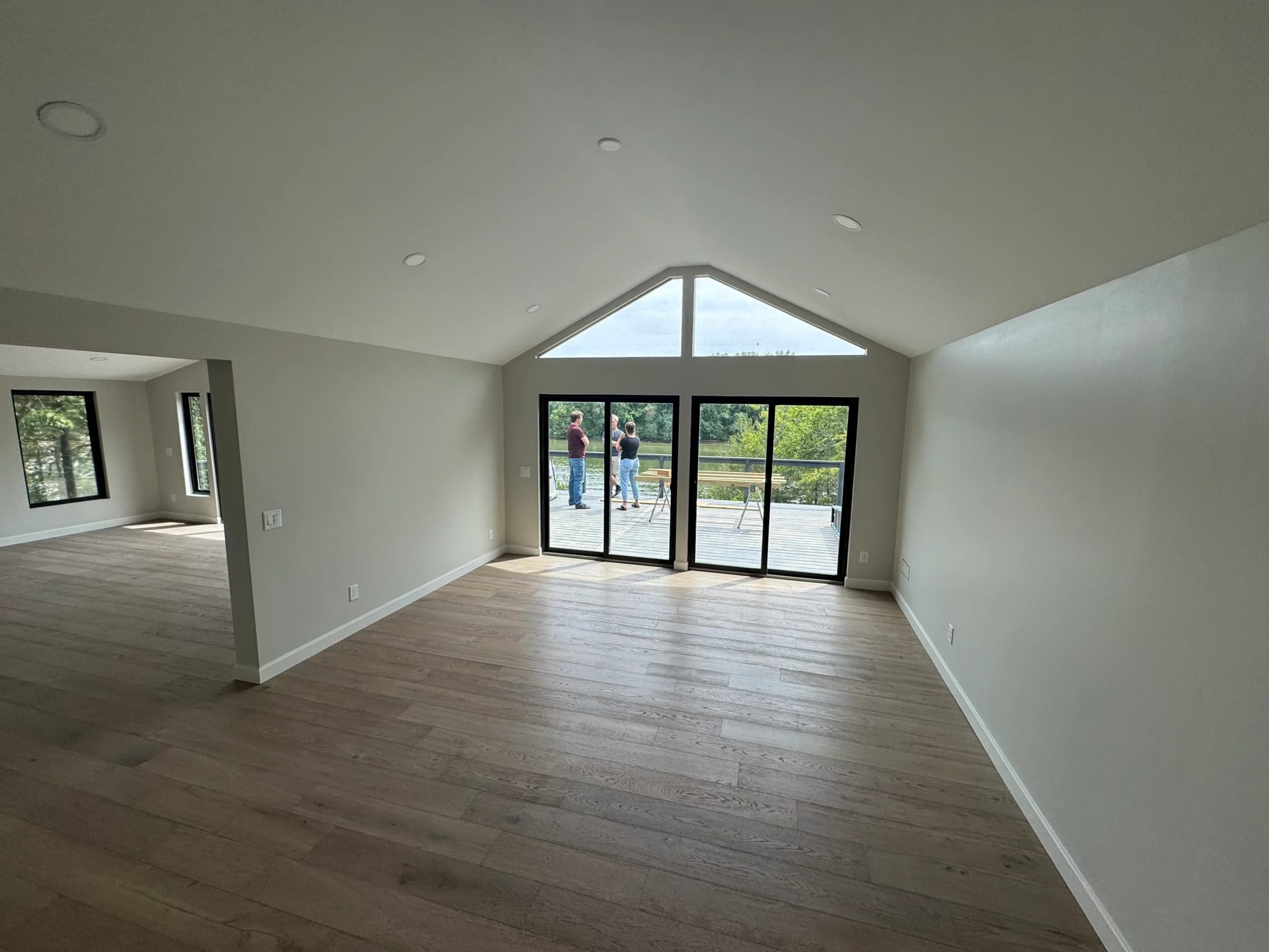 Before staging: empty vaulted living room with wood floors and doors to a deck