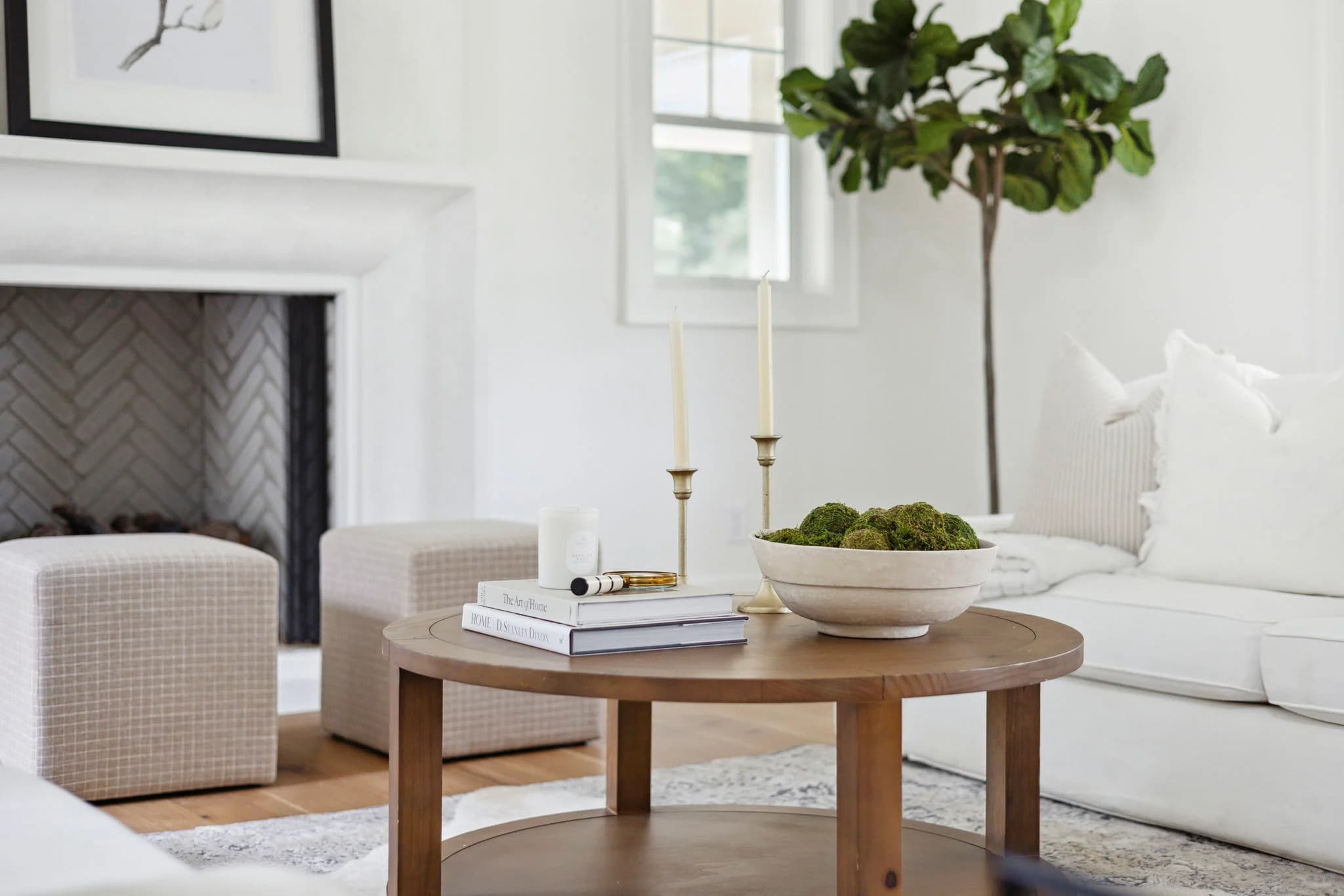 White living room with a round wood coffee table, a white fireplace, and a tall fiddle leaf fig