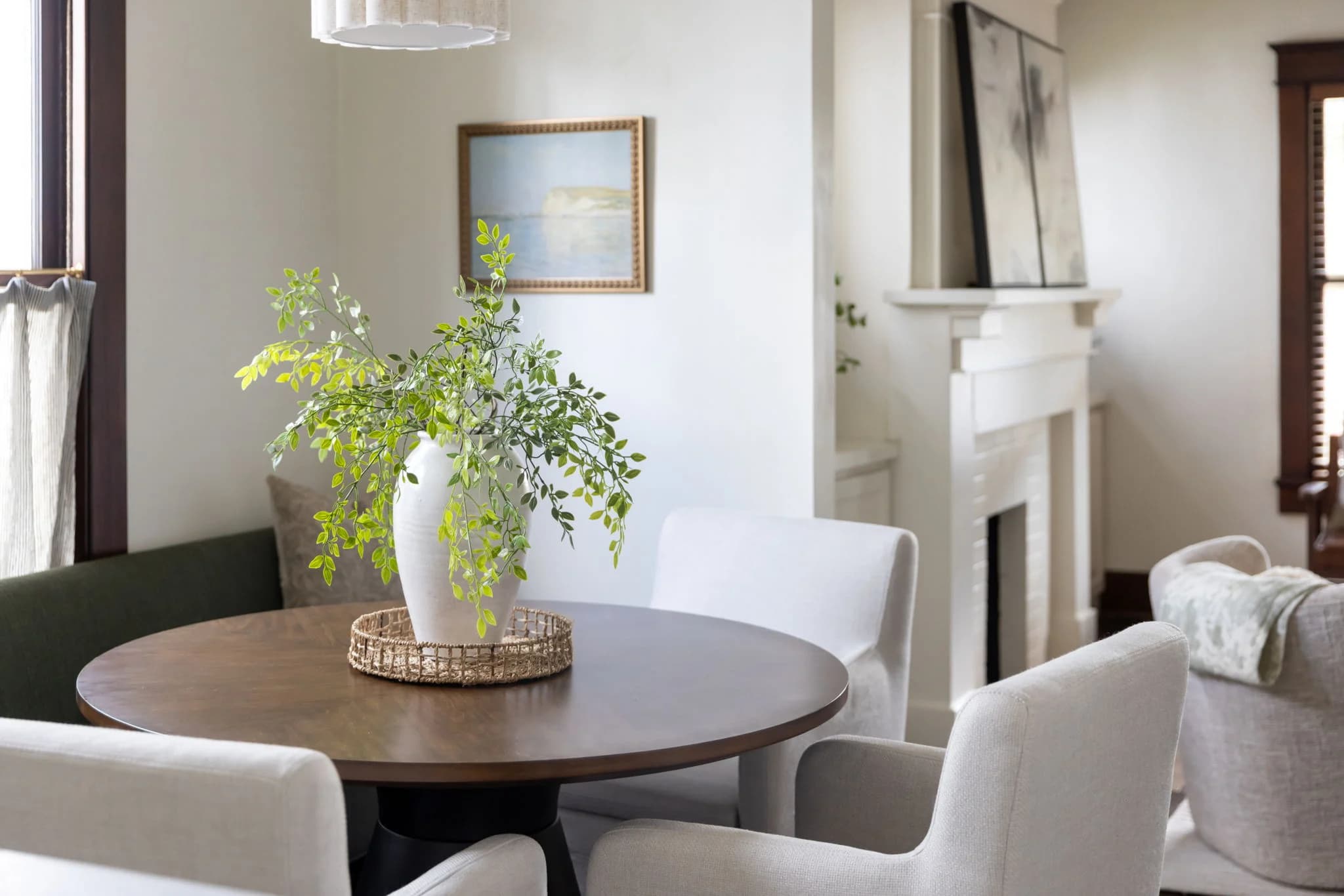 Breakfast nook with a round wood table, cream chairs, and a vase of greenery near a fireplace