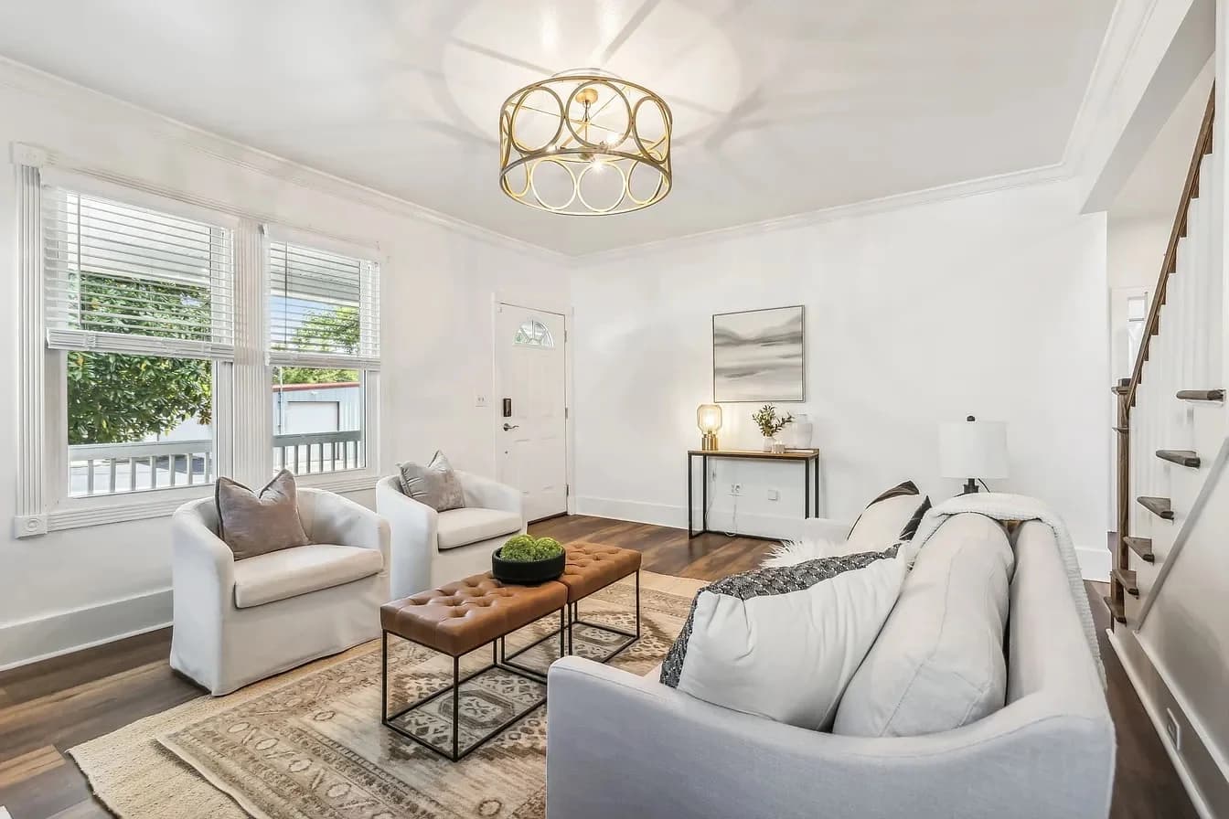 Bright living room with a white sofa, leather tufted coffee table, and gold ceiling fixture