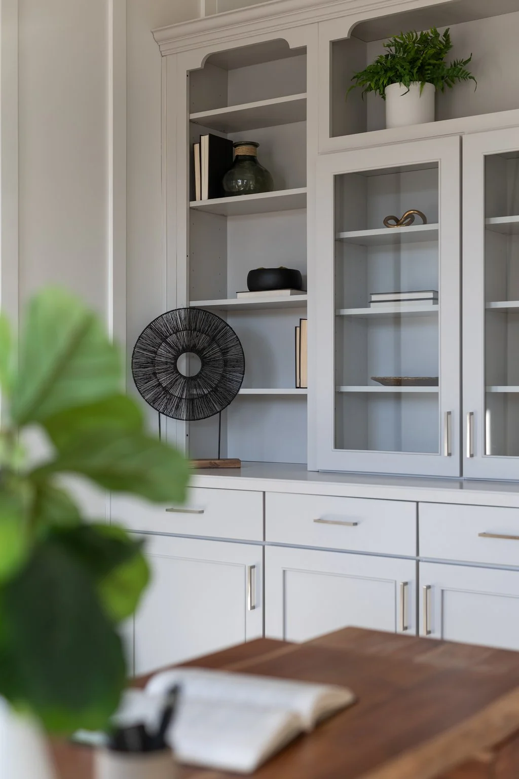 Gray built-in cabinetry with glass doors styled with books and greenery