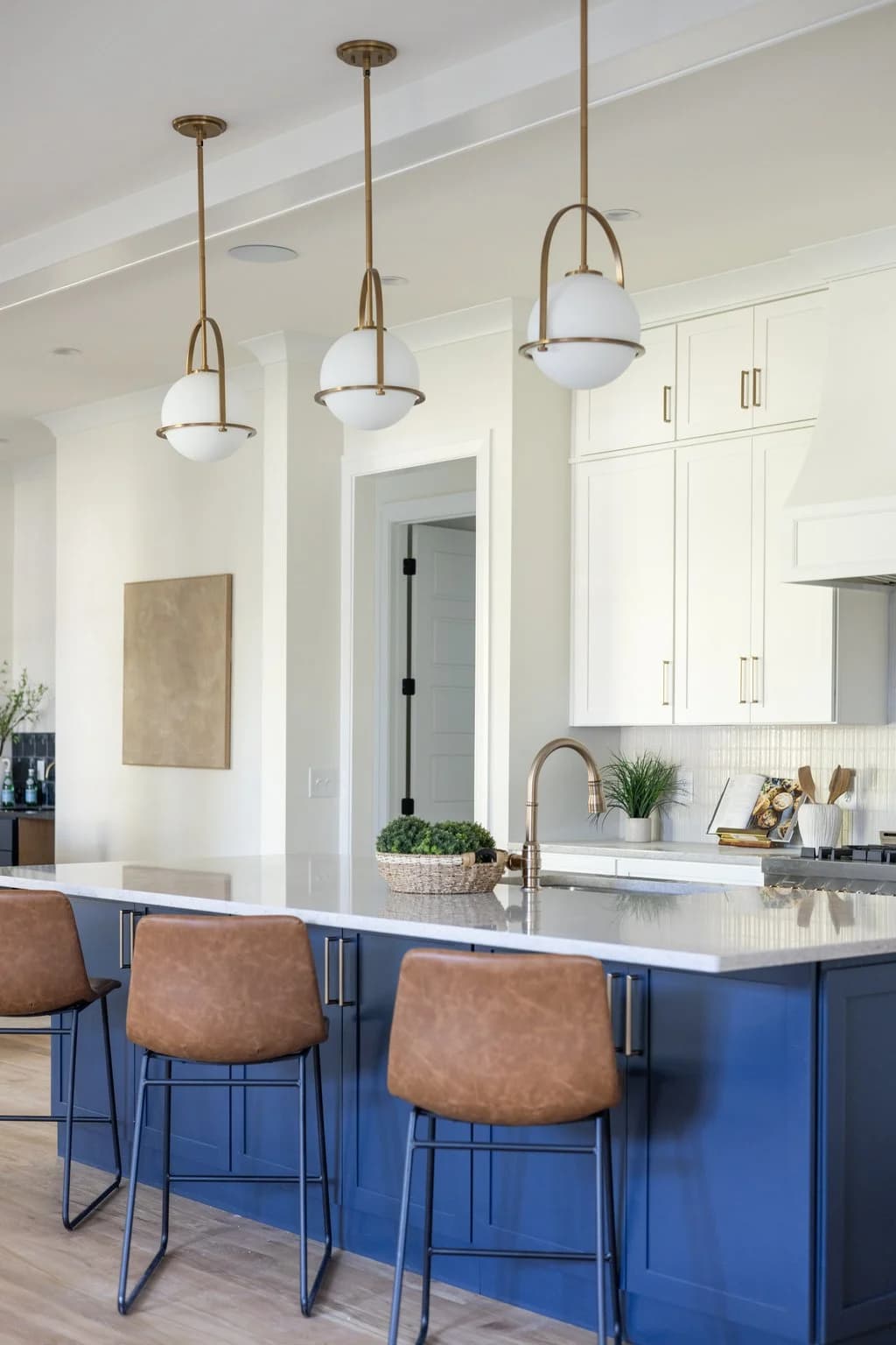 White kitchen with a navy blue island, leather counter stools, and three glass pendant lights