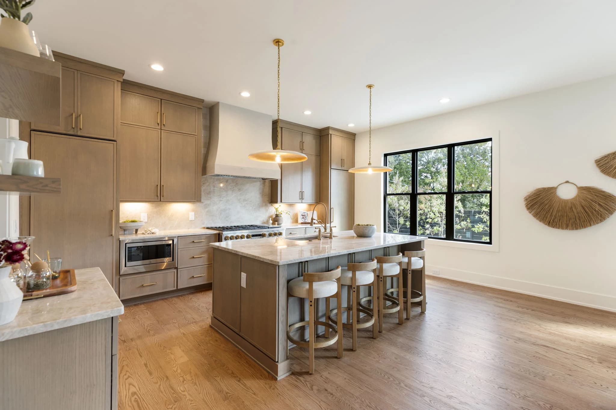 Kitchen with oak cabinets, a plaster range hood, an island with white counter stools, brass pendants, and black framed windows