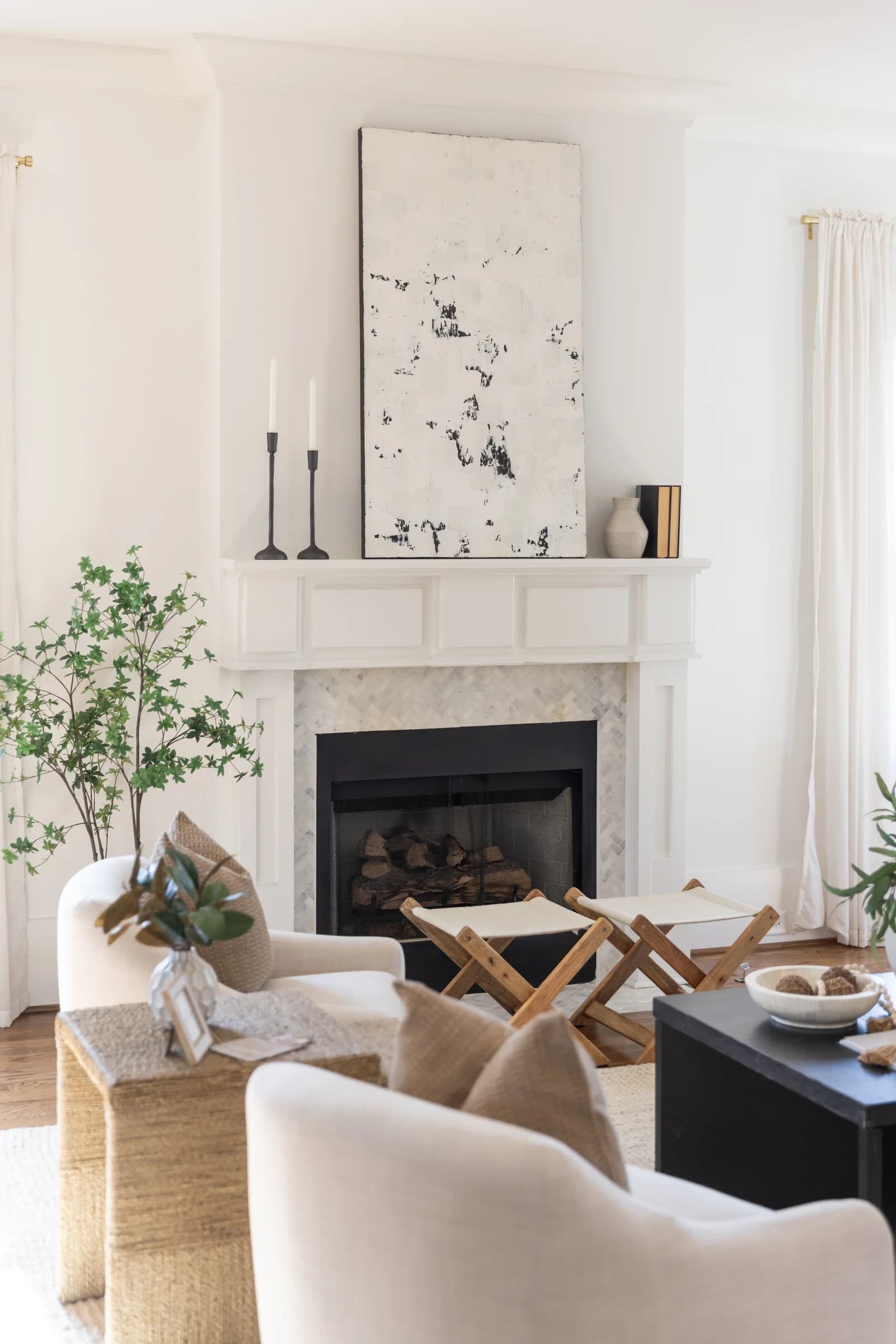Living room with a white fireplace, abstract black and white art, a folding X bench, and cream accent chairs