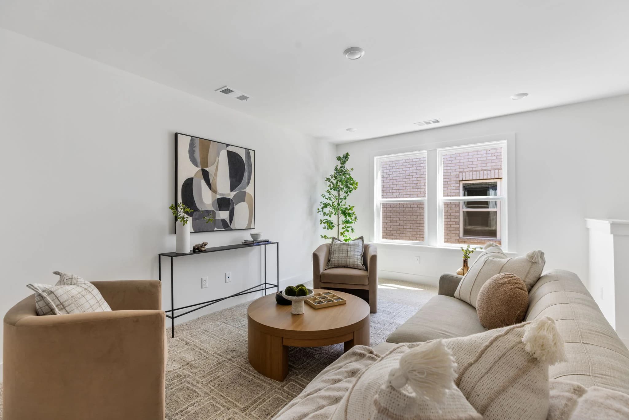 Bright living room with cognac barrel chairs, a round wood coffee table, a cream sofa, and abstract art over a slim console