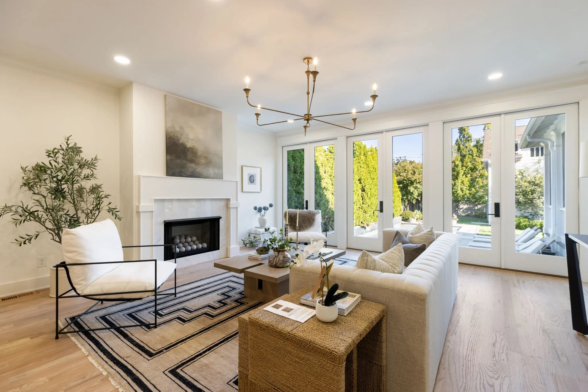 Living room with a white fireplace, a sculptural brass chandelier, French doors, and a black and cream patterned rug