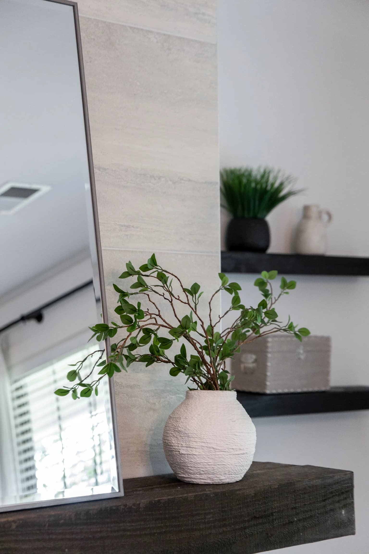 Leaning floor mirror with a vase of branches on a dark wood shelf