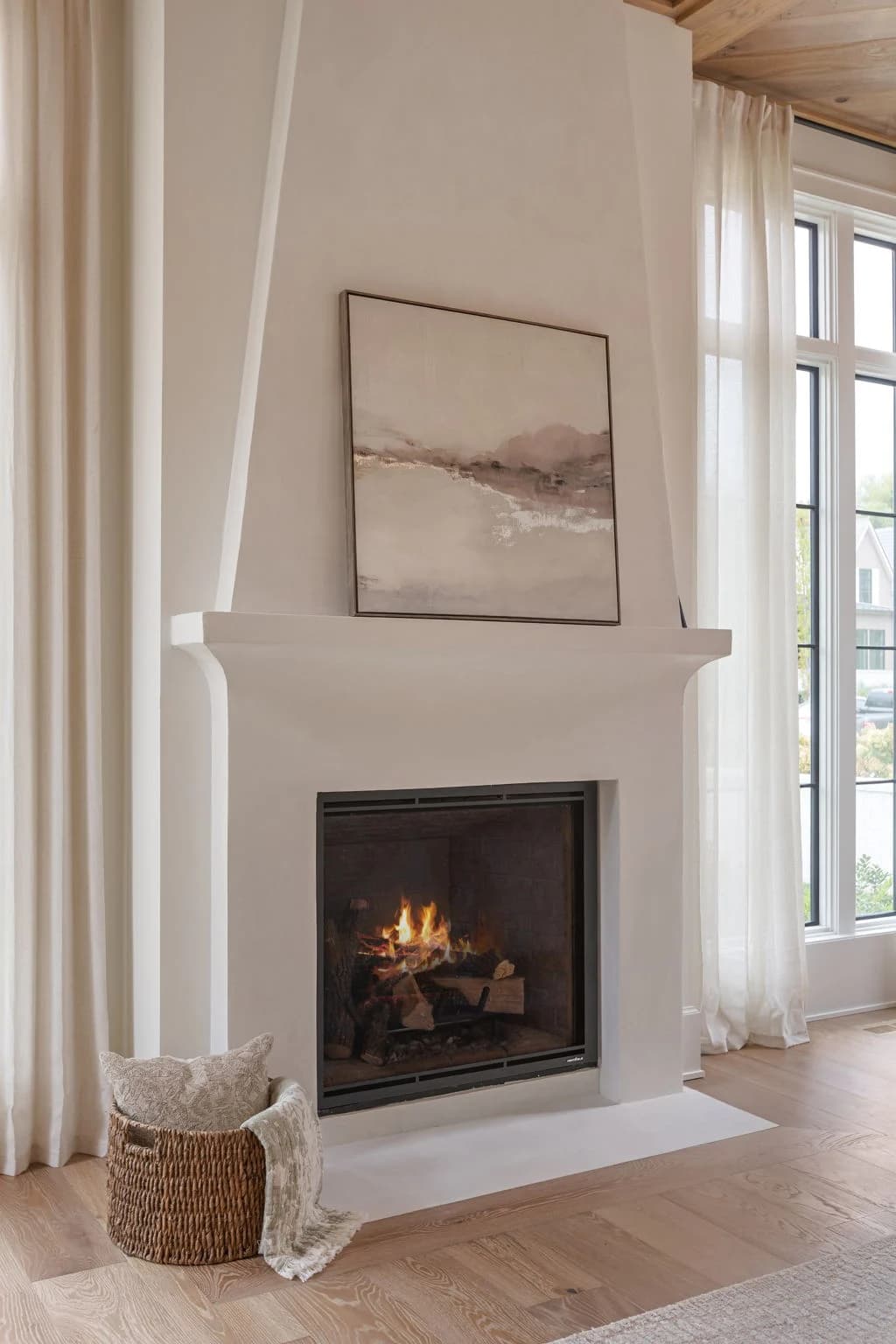 Tall plaster fireplace with a landscape painting above the mantel and sheer linen drapes