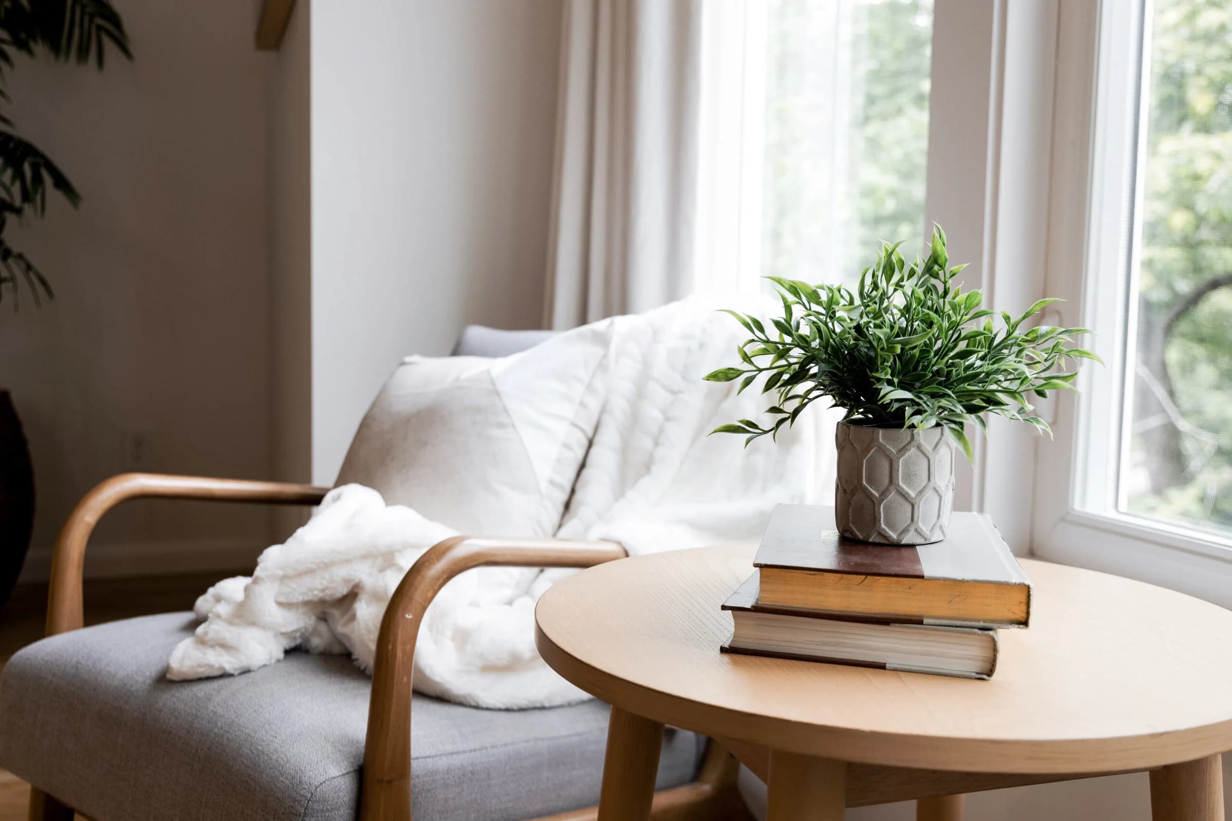 Reading nook with a wood armchair, a white throw, and a round side table with books and a plant