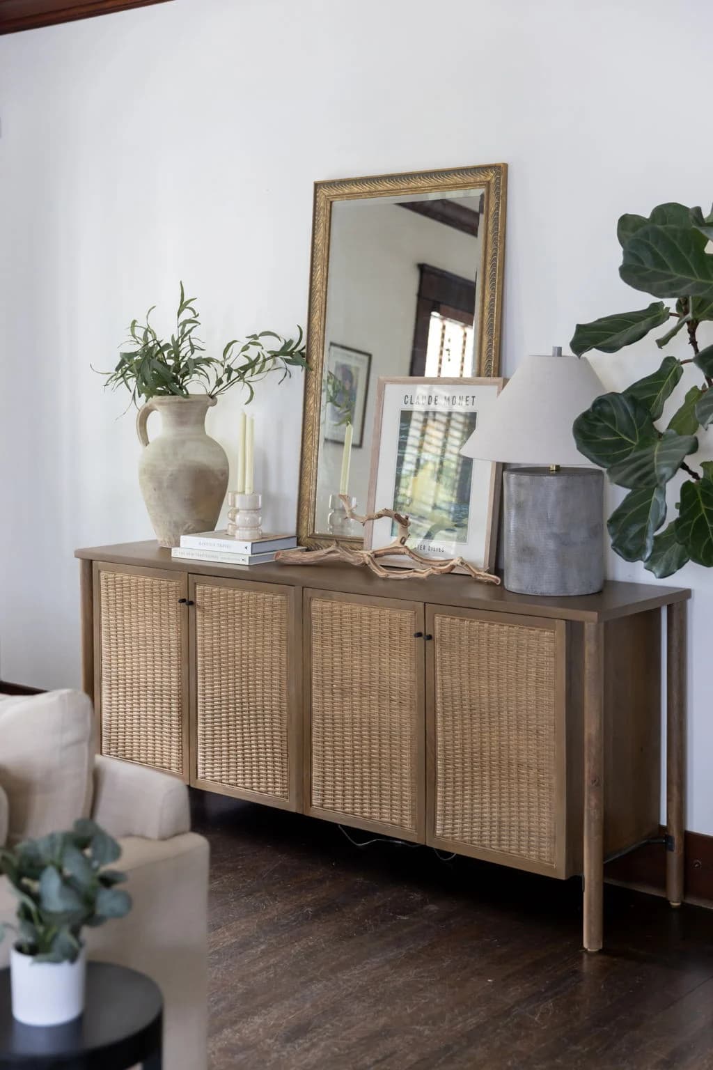 Rattan sideboard styled with a mirror, vases, and books next to a fiddle leaf fig