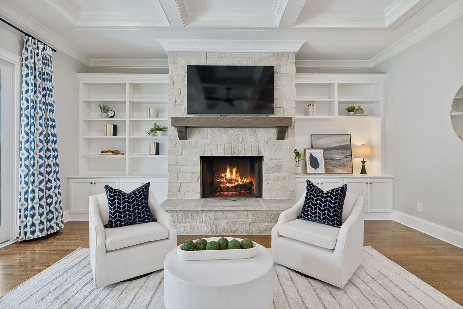 Living room with a stone fireplace, two white swivel chairs, and blue patterned drapes
